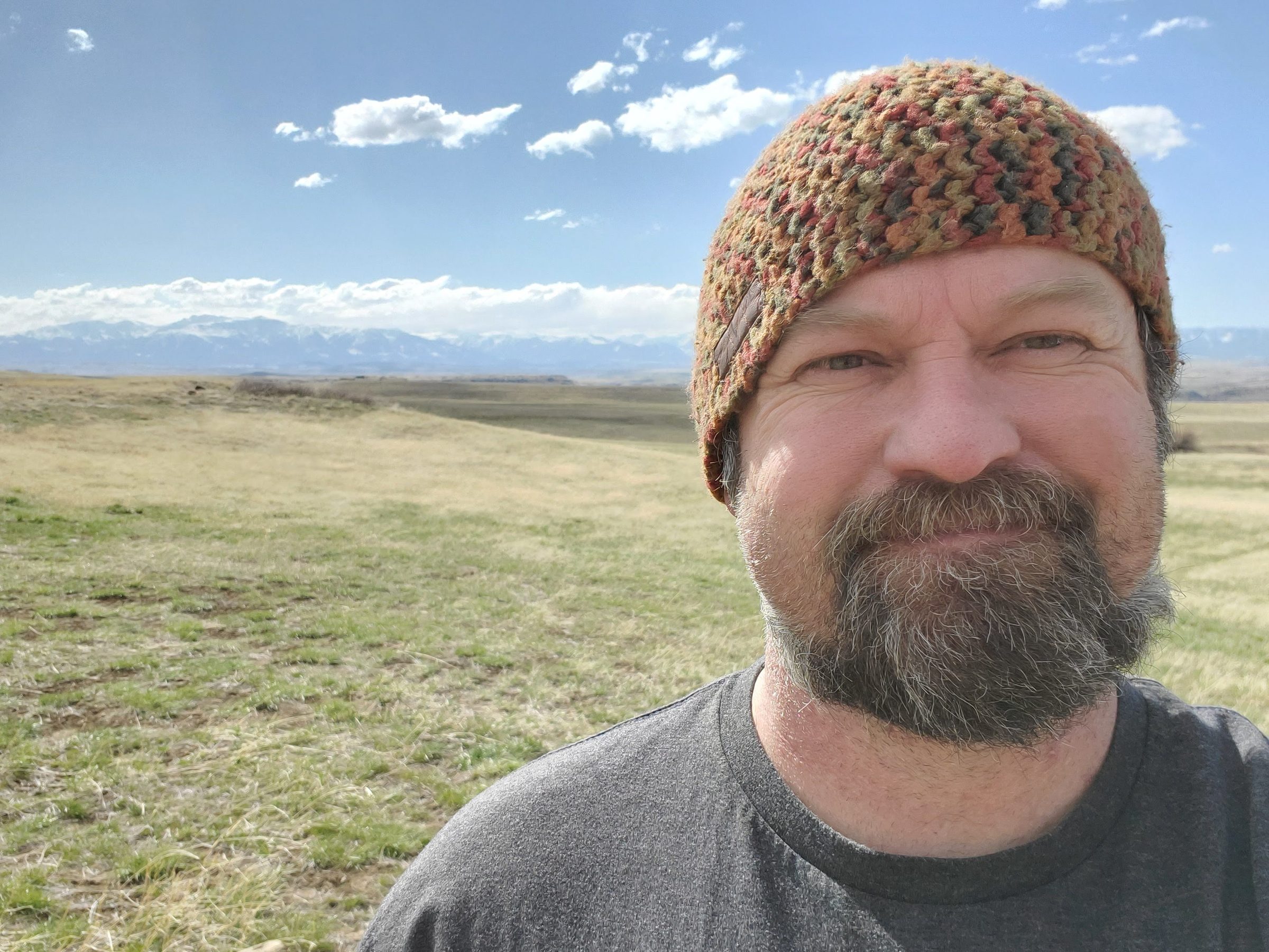 Colter Guthrie, standing outdoors in a knit beanie with Montana grassland and mountains behind him